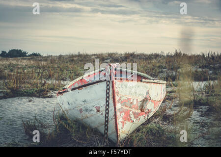 Kleines Boot sitzen am Strand bei Sonnenuntergang ausgeliefert. Alte und verwitterte und verlassen. Stockfoto