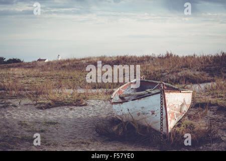 Kleines Boot sitzen am Strand bei Sonnenuntergang ausgeliefert. Alte und verwitterte und verlassen. Stockfoto