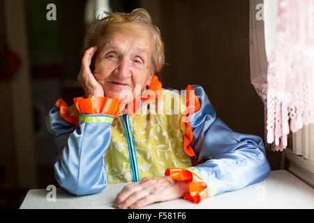 Alte Frau in ethnischen slawische Kleidung sitzt an einem Tisch im Haus. Stockfoto