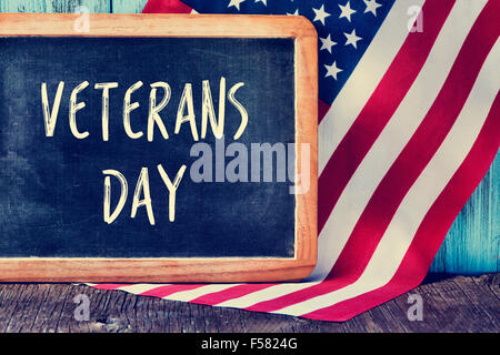 die Text-Veteranen-Tag geschrieben in eine Tafel und eine Flagge der Vereinigten Staaten, auf einem rustikalen hölzernen Hintergrund Stockfoto