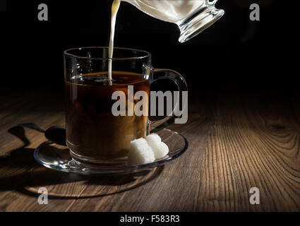 Kaffee in eine transparente Becher, Milch, Löffel und Zucker Stockfoto