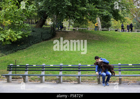Ein Mann hält seinen Hund sitzt auf einer langen Bank im Central Park in Manhattan, New York City, USA Stockfoto