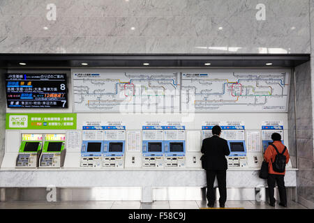 Innenraum der Osaka Station Stadt. Zwei Männer, die an der Bank von self service Automaten, 7 blaue für regelmäßige Züge, zwei grüne für Schnellzüge. Overhead map. Stockfoto