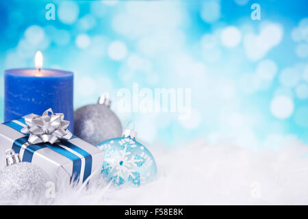 Blau und Silber Weihnachtskugeln, ein Geschenk und eine Kerze auf eine weiche federleichte Oberfläche vor defokussierten blaue und weiße Lichter. Stockfoto