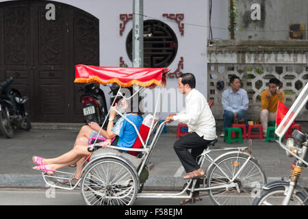 vietnamesische Männchen Cyclo Rikscha Fahrer den Transport von zwei Kunden durch die Straßen von Hanoi Stadtzentrum, Vietnam, Asien Stockfoto