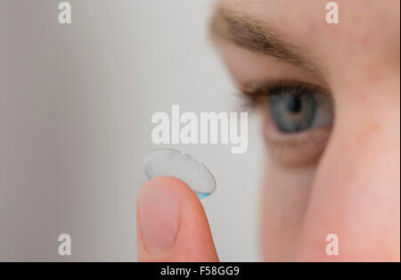 Ein junger Mann balanciert eine Kontaktlinse ist Zeigefinger. Stockfoto