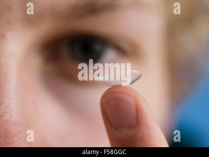 Ein junger Mann balanciert eine Kontaktlinse ist Zeigefinger. Stockfoto