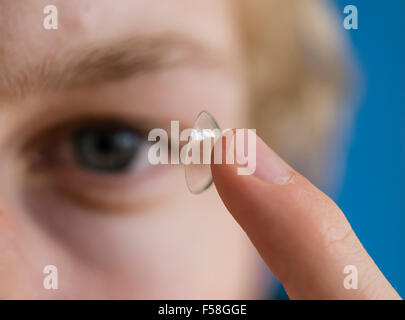 Ein junger Mann balanciert eine Kontaktlinse ist Zeigefinger. Stockfoto