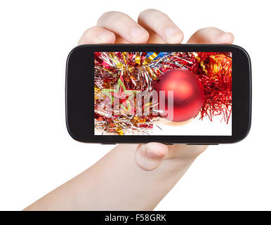 Hand hält Smartphone mit Weihnachtsschmuck auf Bildschirm isoliert auf weißem Hintergrund Stockfoto