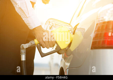Geschäftsmann Pumpen Benzin Kraftstoff im Auto an Tankstelle, goldenen Sonnenlicht Hintergrund hautnah. Stockfoto
