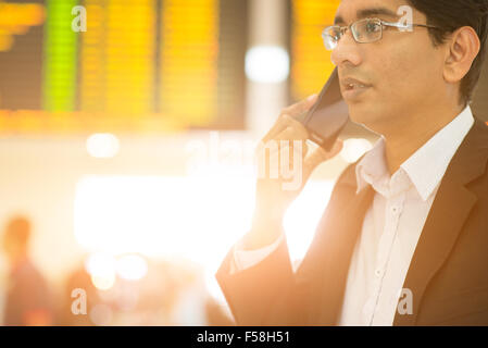 Asiatischen indischen Geschäftsmann am Telefon während seiner Geschäftsreisen, am Flughafen, goldene Sonne heller Hintergrund. Stockfoto