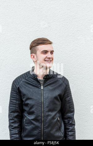 Mittellange Aufnahme, ein junger Mann mit einer Lederjacke hinter einer weißen Wand. Stockfoto