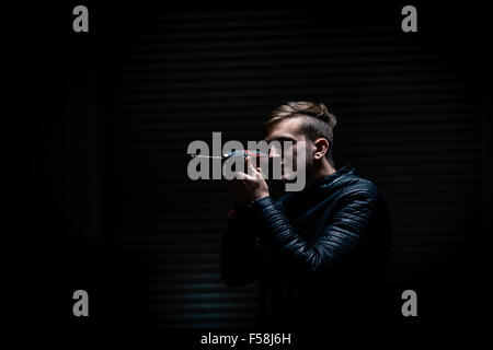 Elektrik Schraubendreher als Waffe verwendet. Ein junger Mann nach einem Schraubendreher, als ob es sich um eine Schusswaffe. Schwarzen Hintergrund. Medium shot, Profil. Stockfoto