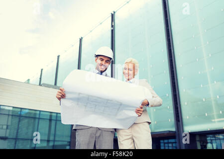 Lächelnde Geschäftsleute mit Bauplan und Helme Stockfoto