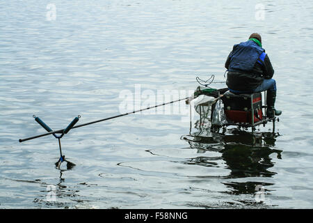 Eine grobe Angeln Angler sitzt auf einer Plattform über ein Loch Stockfoto