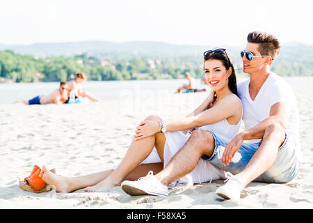 Romantische junges Paar in Liebe sitzen an einem Sandstrand und lächelnd Stockfoto