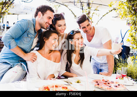 Gruppe von schönen Jugendlichen in einem Restaurant sitzen und dabei das Lächeln auf den Lippen eine selfie Stockfoto