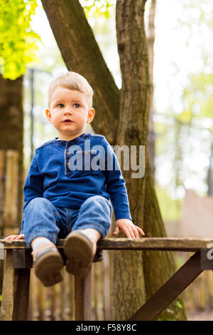 Kleiner hübscher Junge sitzt auf einer Bank im park Stockfoto