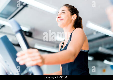 Schöne junge Dame mit dem elliptischen Trainer in einem Fitnessstudio in eine positive Stimmung Stockfoto