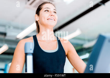 Schöne junge Dame mit dem elliptischen Trainer in einem Fitnessstudio in eine positive Stimmung Stockfoto