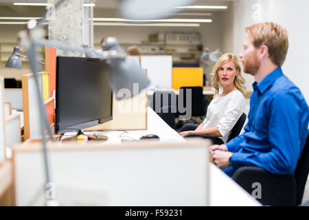 Schöne blonde sitzen in einem Büro arbeiten und im Gespräch mit einem Kollegen Stockfoto