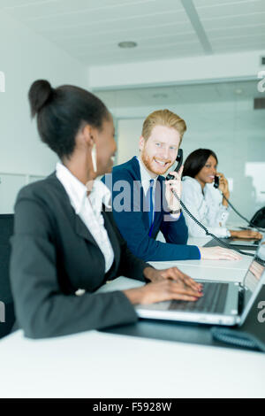 Eine schöne, schwarze, junge Frau mit ihrem roten Haird-Kollegen im Gespräch mit einem Kunden in einem Callcenter in einem Büro arbeiten Stockfoto