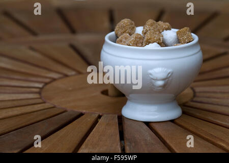 Braune und weiße Stück Würfelzucker in einer Keramikschale auf einem runden Holztisch Stockfoto