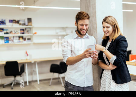 Zwei Kollegen lächelnd beim Betrachten des Telefons in einem wunderschönen Büro Stockfoto