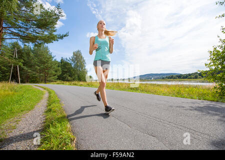 Motivierte Frau läuft schnell auf einer Straße im Wald Stockfoto