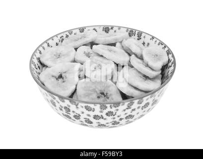 Getrocknete Bananen-chips in einer Porzellanschüssel mit floralem Design, isoliert auf einem weißen Hintergrund - monochrome Verarbeitung Stockfoto