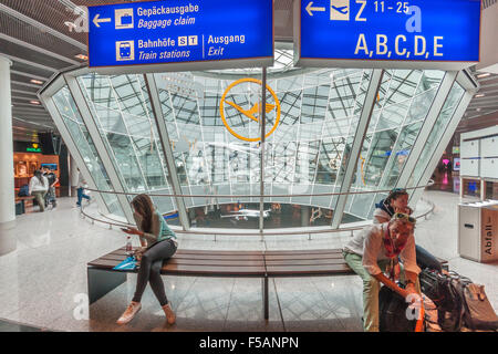 Frankfurt am Main, Deutschland. Menschen am Flughafen warten. Große "Lufthansa"-Logo im Hintergrund. Stockfoto