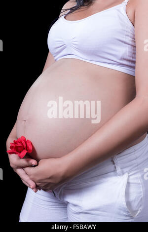 Schwangere Frau streichelt ihren Bauch mit einer roten Blume in der hand Stockfoto