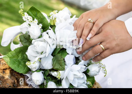 weißen Blumenstrauß auf einem Felsen und Bräutigam die Hände übereinander mit ihre Eheringe seit Stockfoto