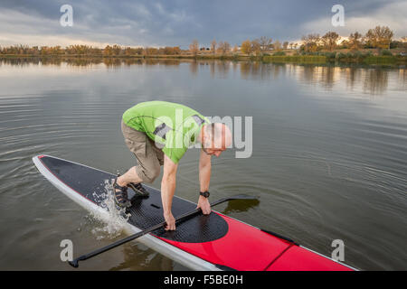 Senioren männlich startet paddeln Training auf seinem Stand up Paddleboard auf einem See in Colorado Stockfoto