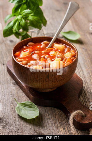 Bohnensuppe in einer Holzschale, Basilikum und Löffel auf alten hölzernen Hintergrund Stockfoto