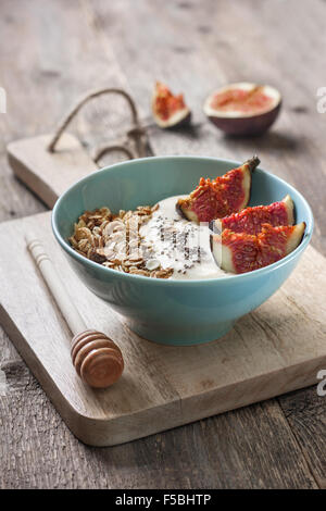 Frühstück mit Müsli, Joghurt, Feigen und Chia-Samen in einer blauen Schüssel auf einem hölzernen Hintergrund Stockfoto