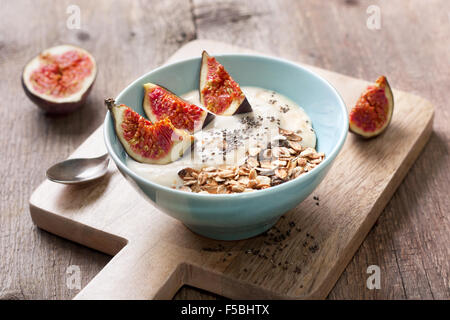 Frühstück mit Müsli, Joghurt, Feigen und Chia-Samen in einer blauen Schüssel auf einem hölzernen Hintergrund Stockfoto