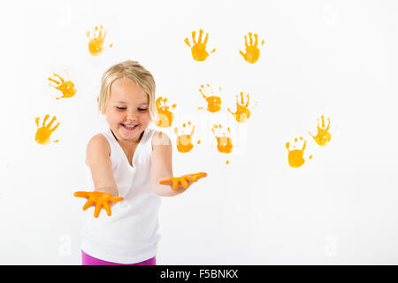 Kleine Mädchen malen weiße Wand mit orange Farbe und Handabdrücke Stockfoto