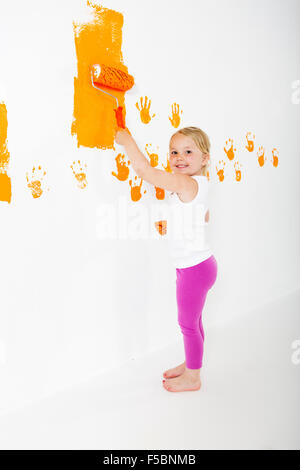 Kleine Mädchen malen weiße Wand mit orange Farbe Stockfoto