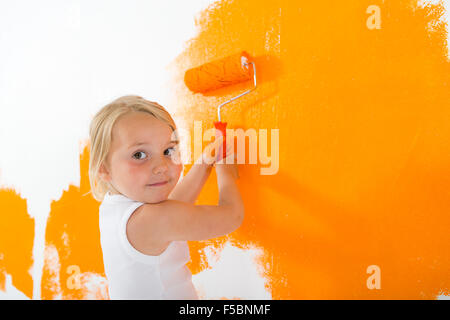 Kleine Mädchen malen weiße Wand mit orange Farbe Stockfoto