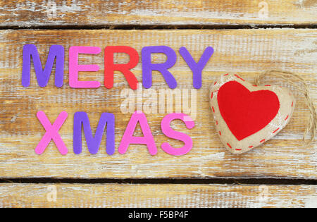 Frohe Weihnachten auf Oberfläche und rote gestrickte Herz aus Holz mit bunten Buchstaben geschrieben Stockfoto