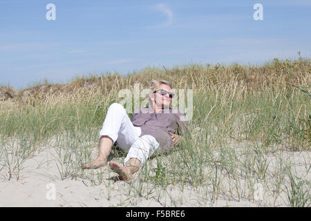 Ein Senior in den Dünen auf einem Strand und schaut in die Ferne liegend Stockfoto