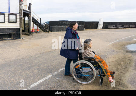 Eine 95 Jahre alte Frau mit ihrem Betreuer oder Helfer auf der Mole in Broadstairs, gut verpackt gegen die Kälte an einem strahlenden Herbsttag. Stockfoto