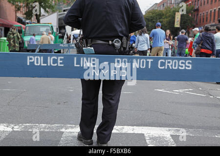 Männliche NYPD Police Officer lehnt sich an eine Barriere, die Leute auf der Straße Messe auf der Atlantic Avenue in Brooklyn zu beobachten Stockfoto