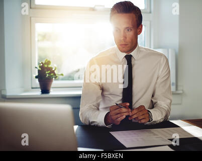 Professionelle Business-Mann im Büro an seinem Schreibtisch arbeitet, hält einen Stift und mit Blick auf seinen laptop Stockfoto