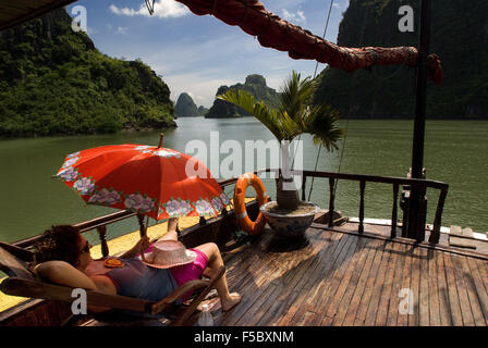 Touristen, die Entspannung in einer chinesischen Dschunke, Halong Bay touristischen Bootstour, Vietnam. Dschunke, Segeln unter Karst Kalkstein Berg Stockfoto