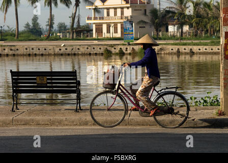 Radfahrer-Frau auf der Promenade am Thu Bon Fluss in Hoi An Vietnam. Typischen Vietnamesischen Frau mit Hut. Stockfoto