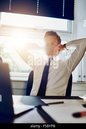 Junges Unternehmen Mann Unternehmer Überstunden in seinem Büro Blick auf seinen Computer mit Armen hinter seinem Nacken Stockfoto