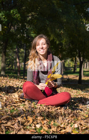 Glückliches Brünette Mädchen sitzen im Park unter den gelben Herbst Blätter Stockfoto