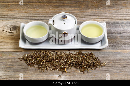 Tee-Server mit Keramikbechern, Topf, Tablett und trockener grüner Tee Blätter auf rustikalen Holz. Stockfoto